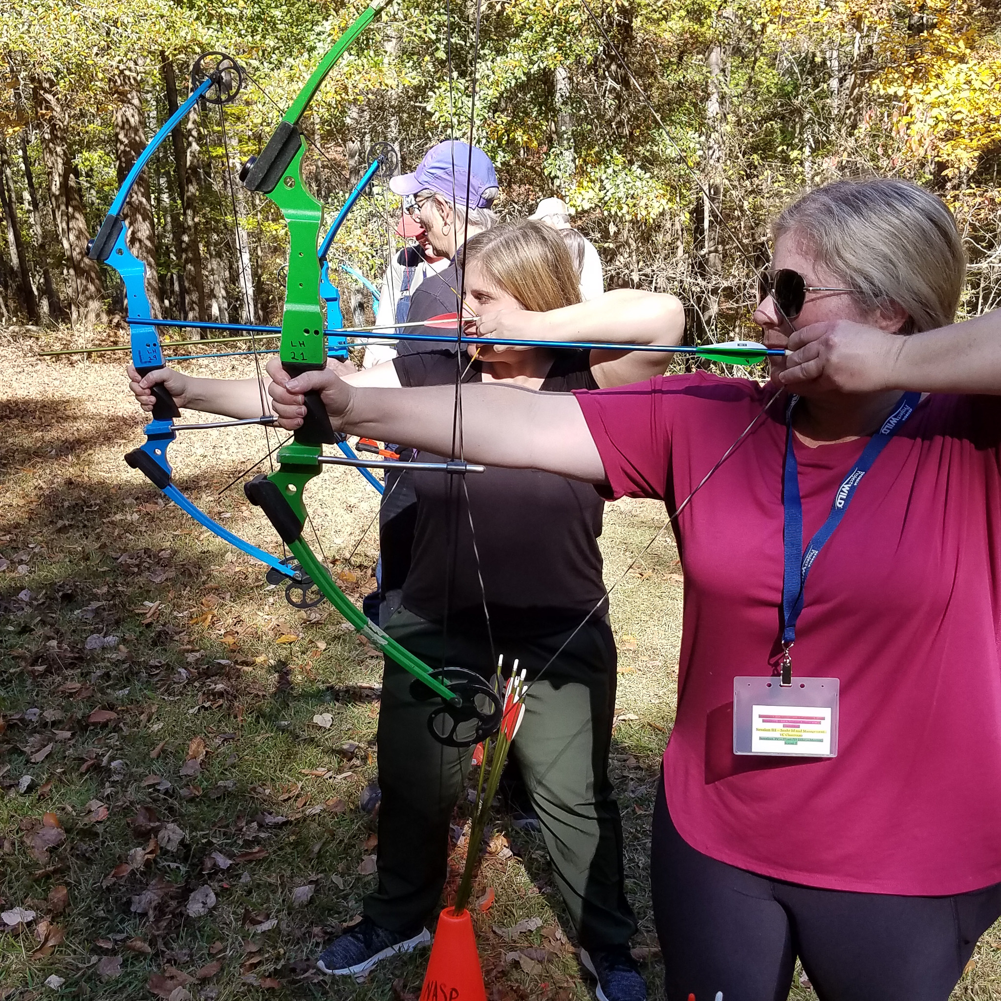 Two young women stand with archery bows drawn.
